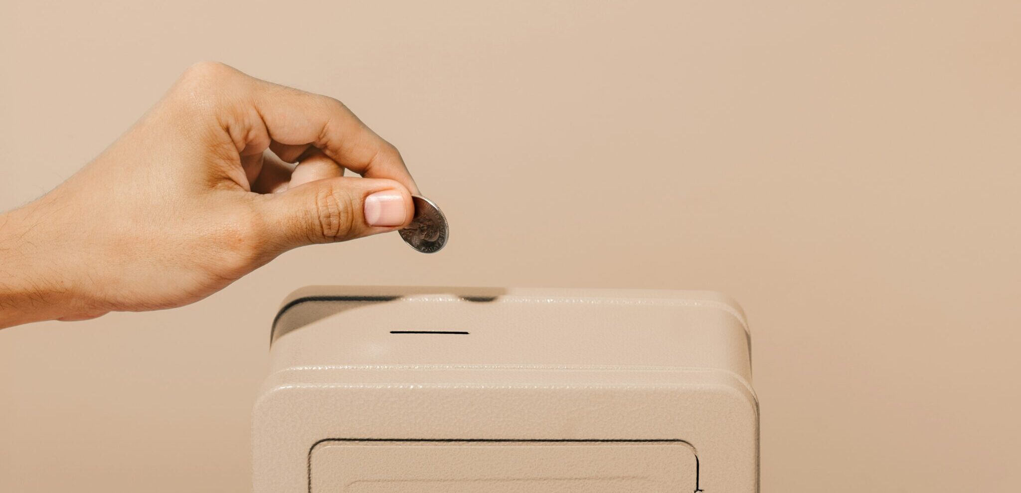 Eine Hand die eine Münze in einen Safe steckt